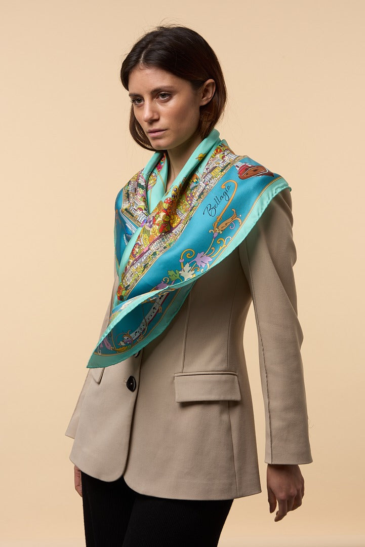 woman with cream coat wearing a blue silk scarf depicting the town of Bellagio