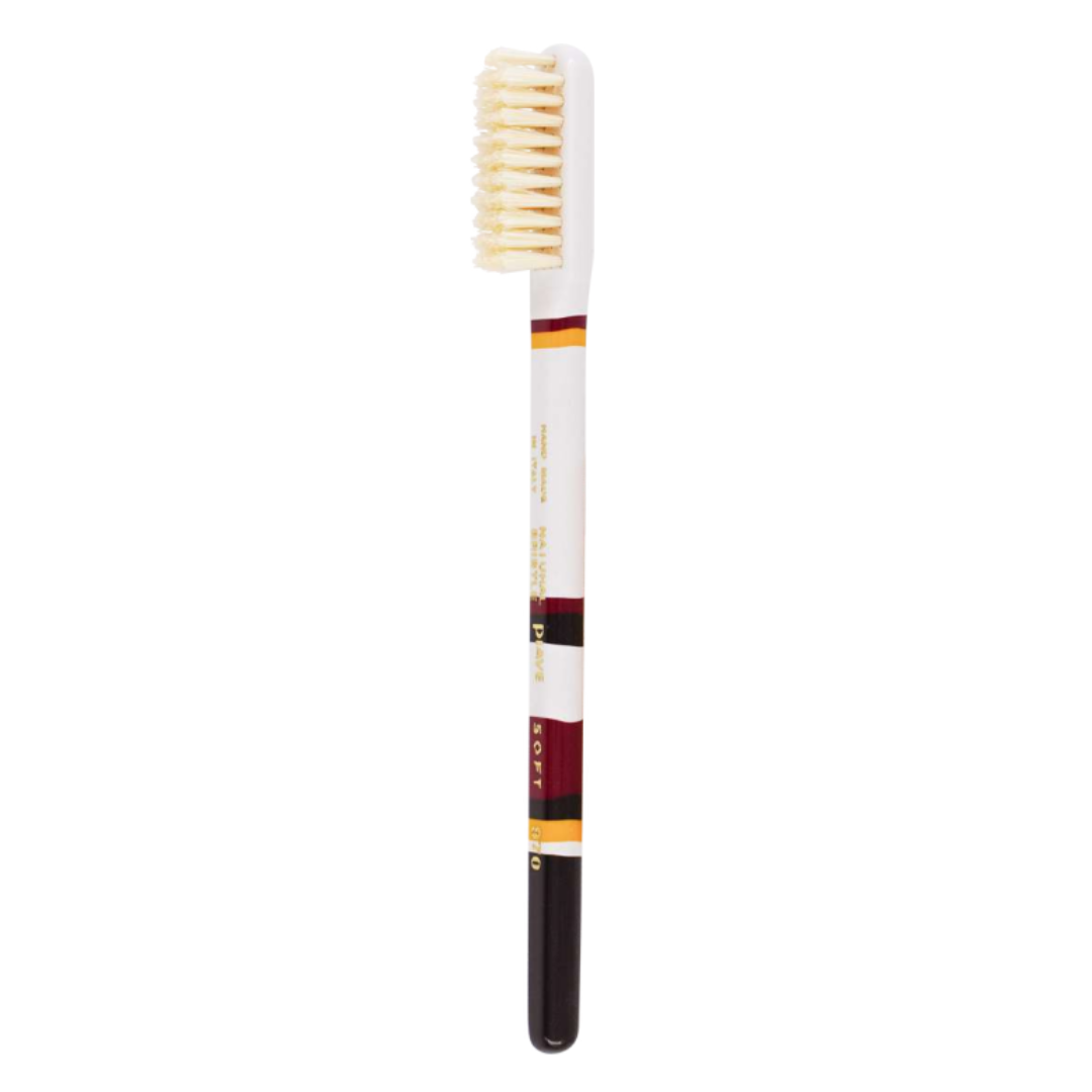 A single manual toothbrush with a white handle, cream-colored bristles, and decorative bands of burgundy, gold, and black on the handle, shown against a plain white background.