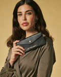 Woman holding a black wallet with a gold brand logo against a beige background
