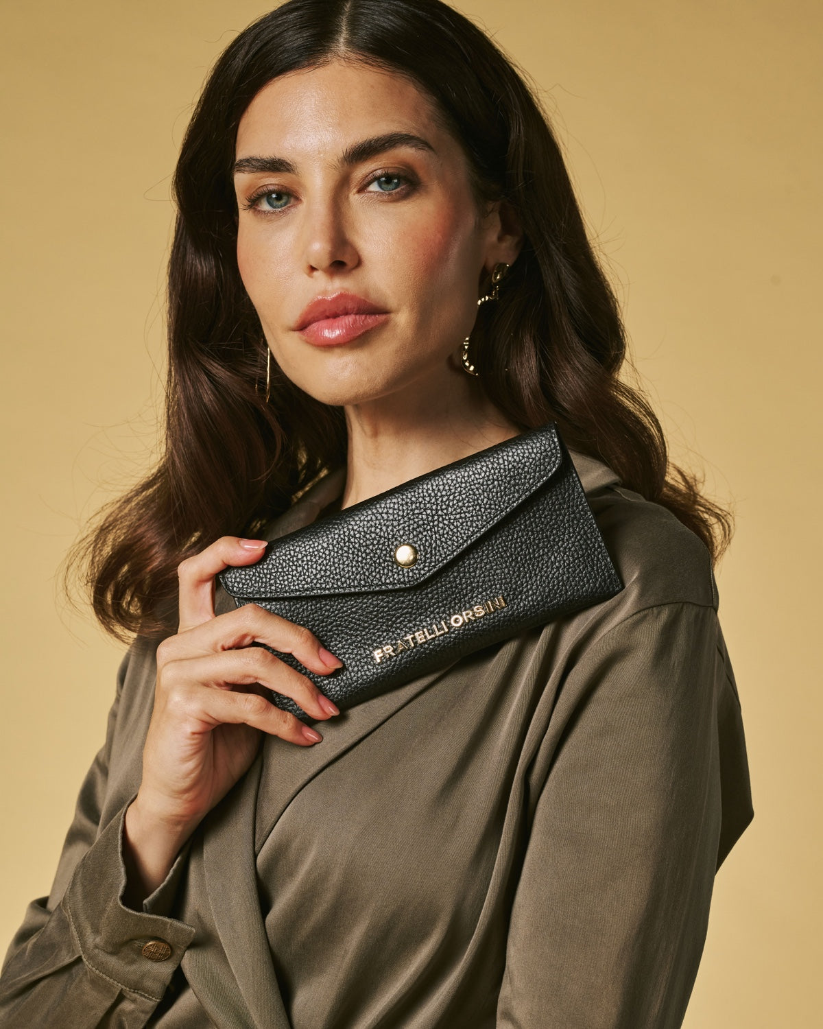 Woman holding a black wallet with a gold brand logo against a beige background