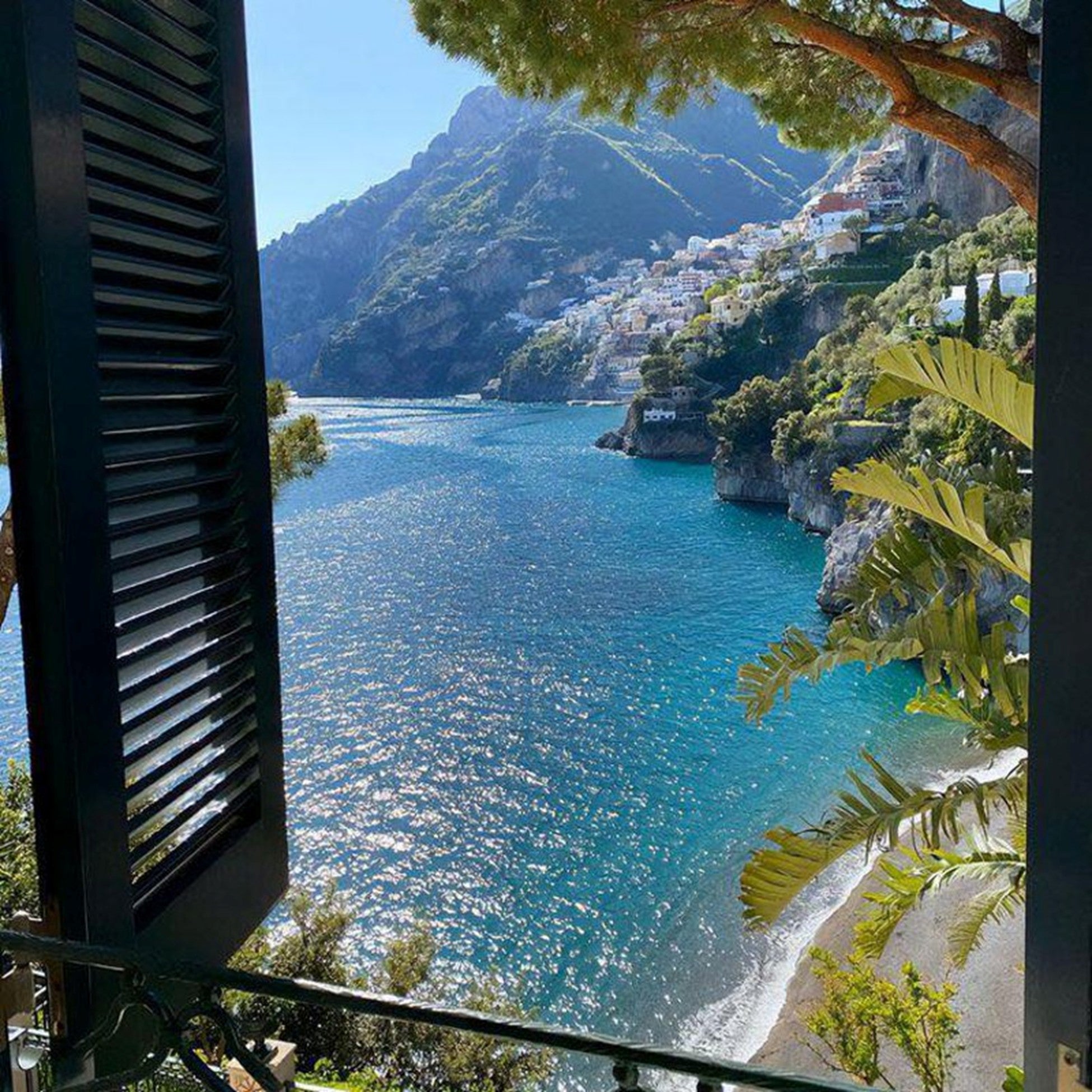 Scenic view of a coastal town with blue water and green mountains, framed by architectural elements.