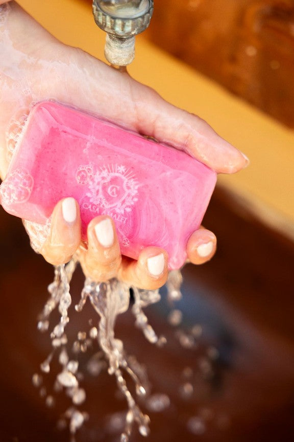 Pink bar of soap being held under running water with a blurred background