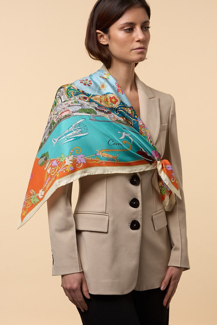 woman wearing a cream jacket and a silk scarf depicting the town of Como on her shoulder