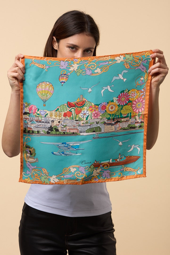 brunette woman holding a colourful silk scarf depicting the city of Como