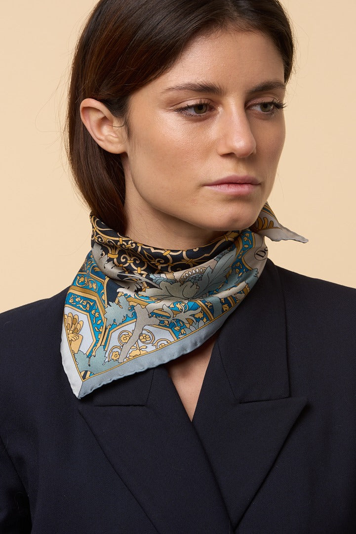 brunette woman with blue jacket and blue, white and gold silk scarf on her neck
