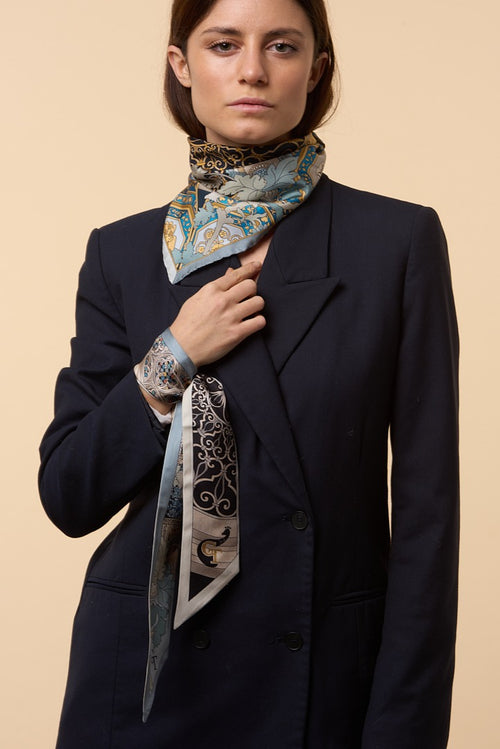 brunette girl with blue coat, blue and black silk scarf on the neck, and blue and black twilly on the wrist