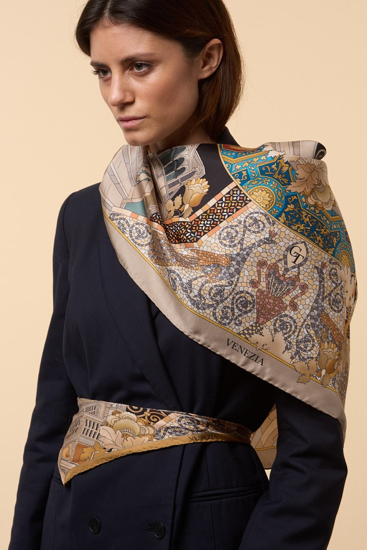 brunette woman with blue jacket and golden scarf with mosaics on her shoulder and waist