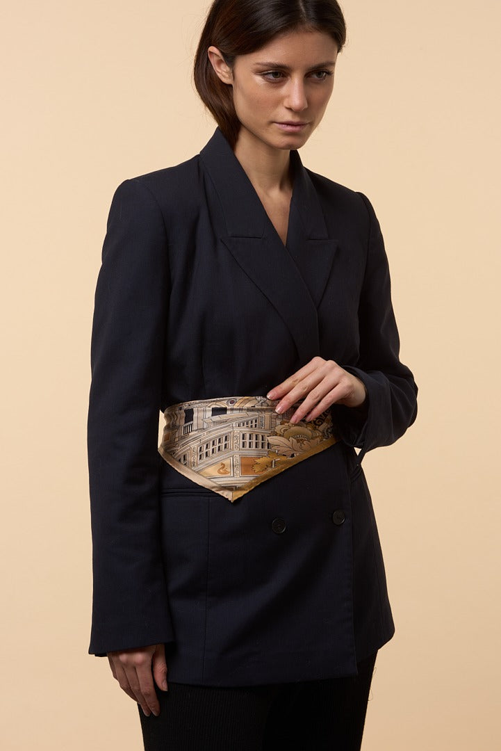 brunette woman with blue coat and golden silk scarf on her waist used as a belt