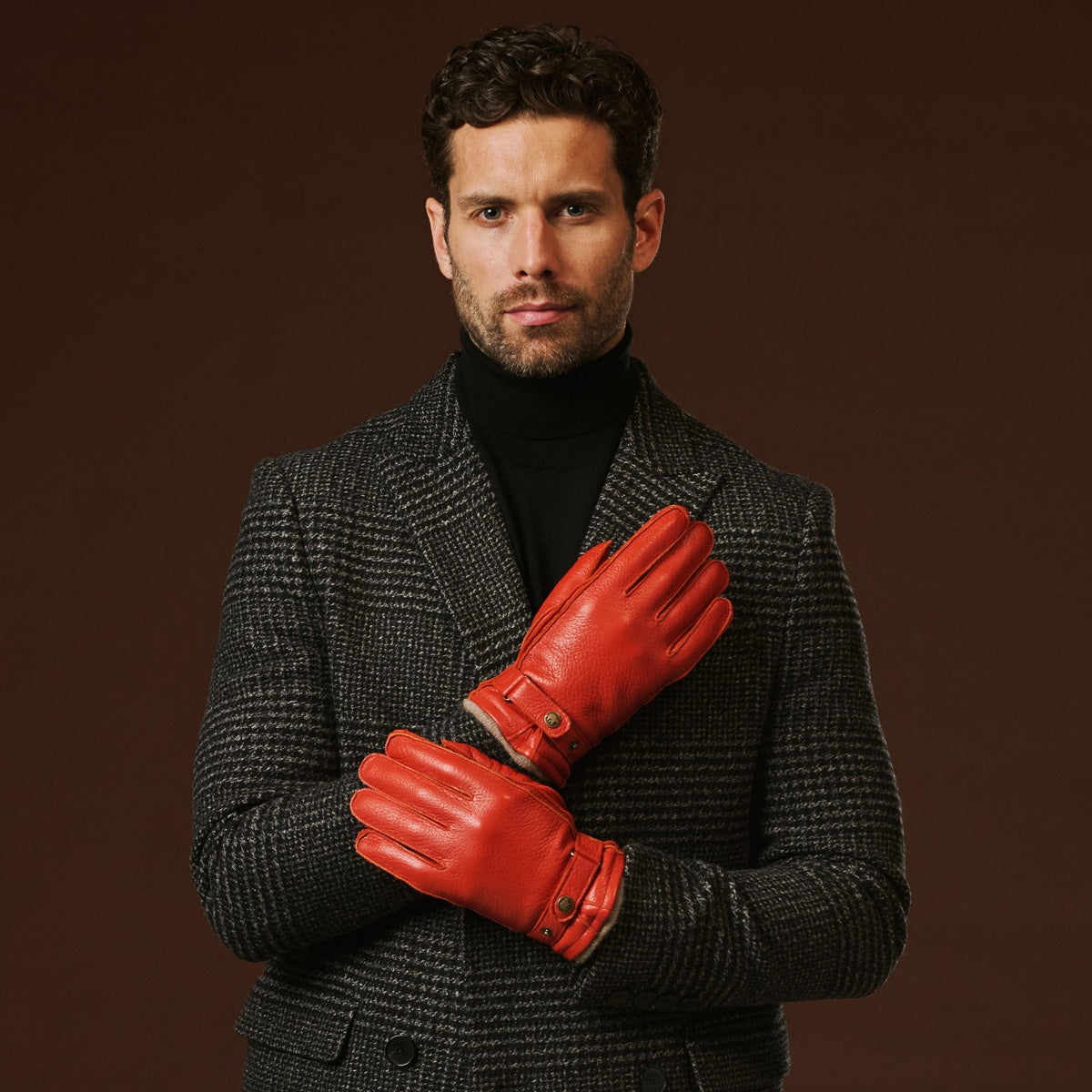 Man wearing a dark coat and red gloves against a brown background