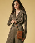 Woman wearing a green trench coat holding a brown leather bag against a beige background