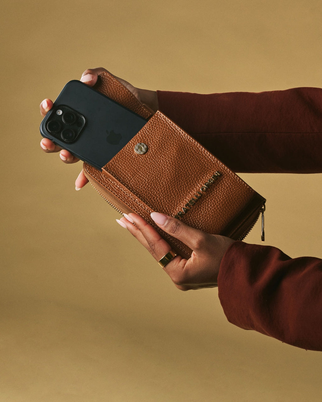 Person holding a brown leather wallet with a phone case on a beige background
