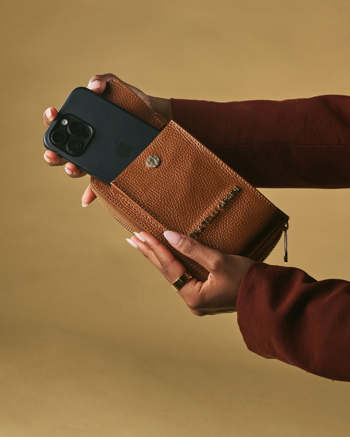 Person holding a brown leather wallet with a phone case on a beige background