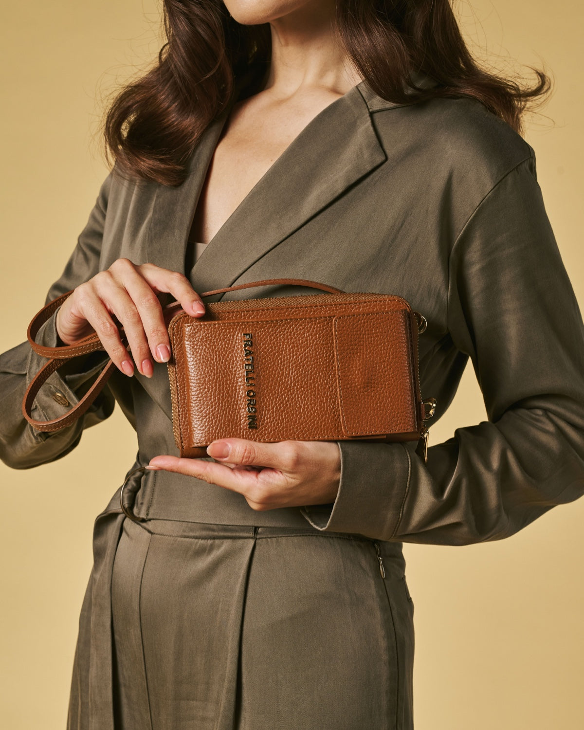 Person holding a brown leather bag against a beige background
