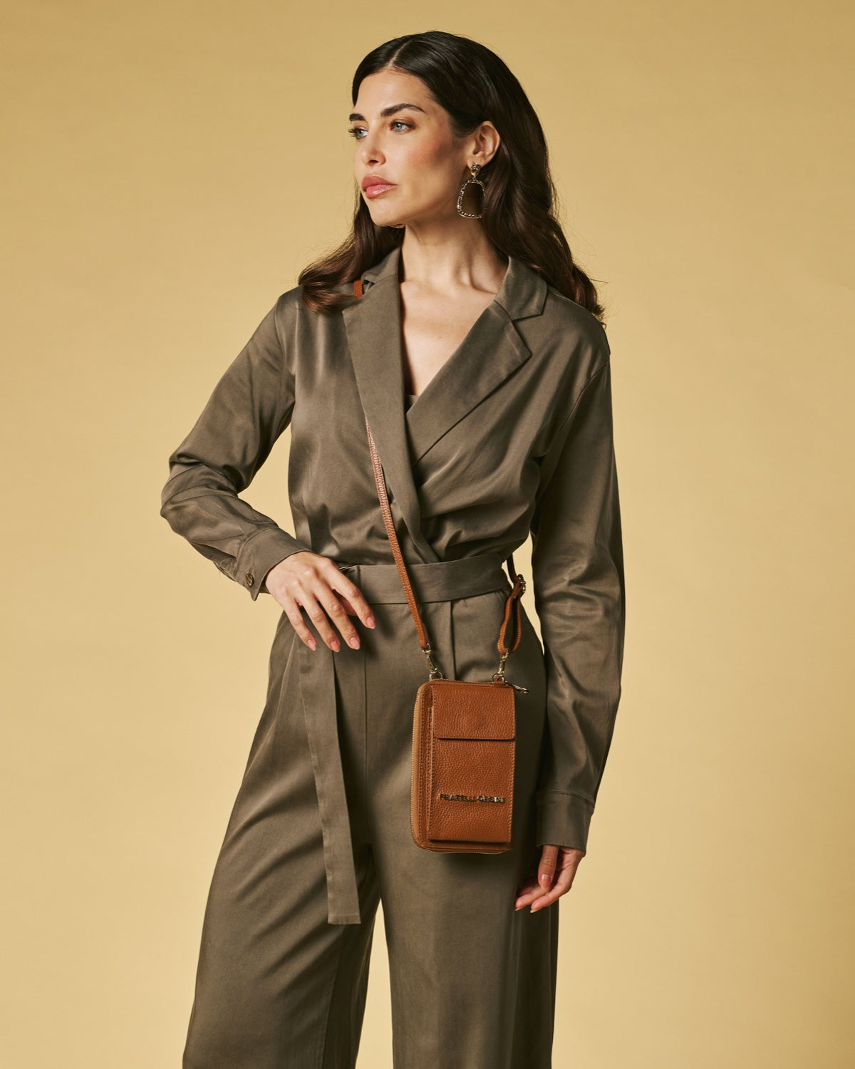 Woman wearing a green trench coat with a brown leather bag on a beige background