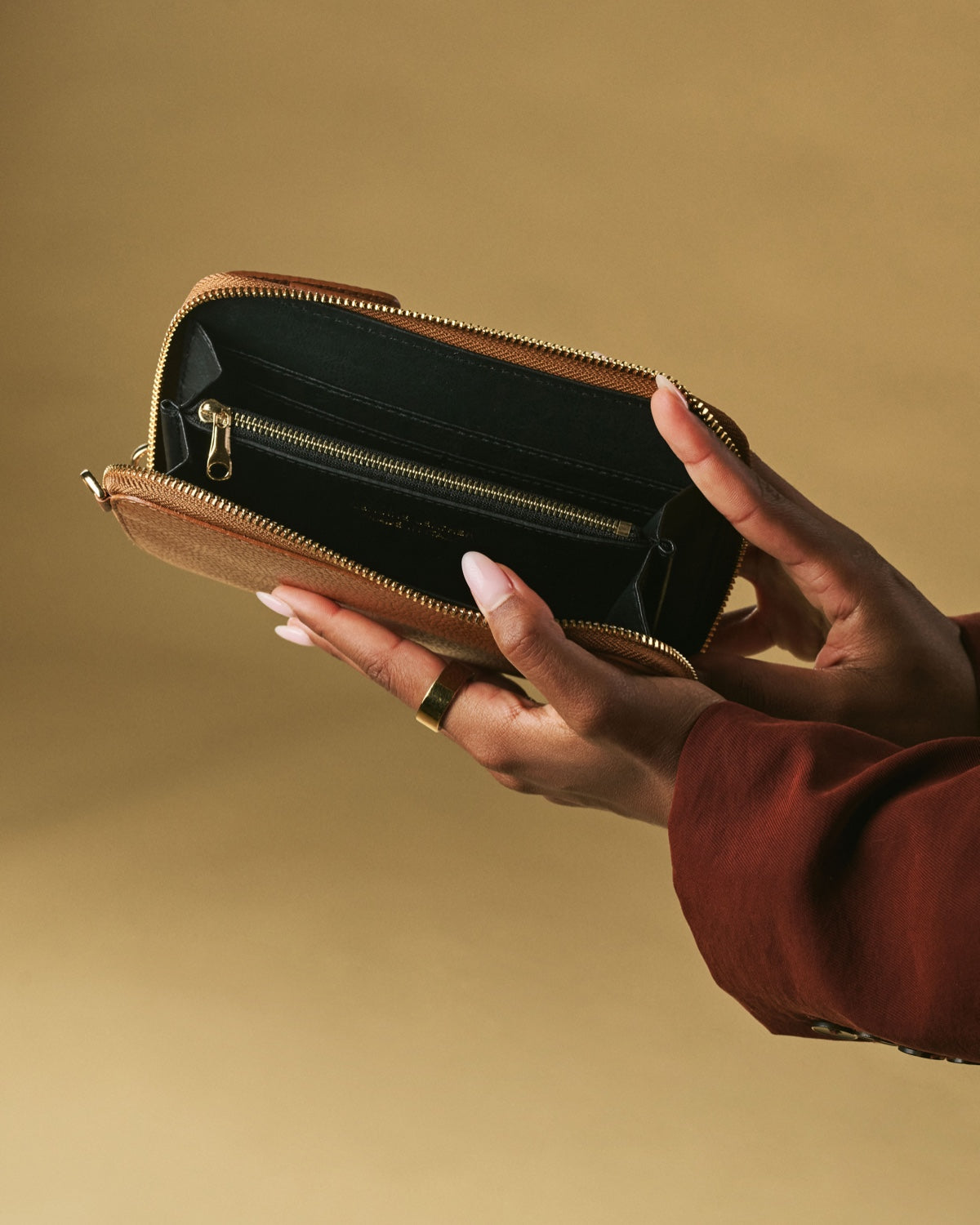 Brown leather wallet held by a hand against a beige background