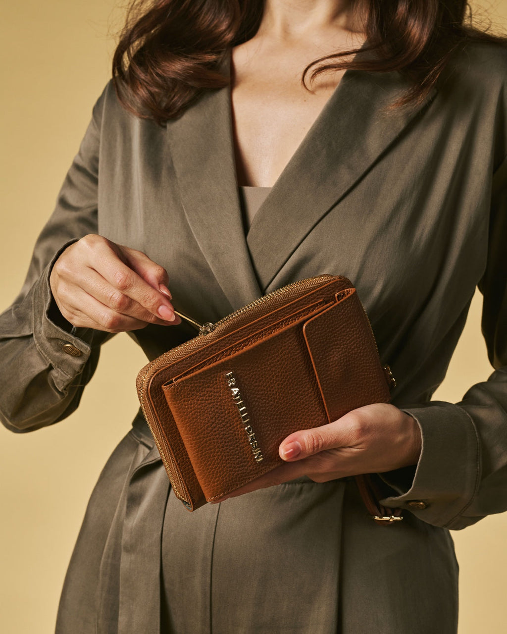 Person holding a brown leather wallet with a beige background