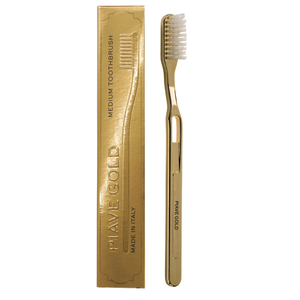 A gold toothbrush with white bristles displayed next to its matching gold packaging box on a plain white background.