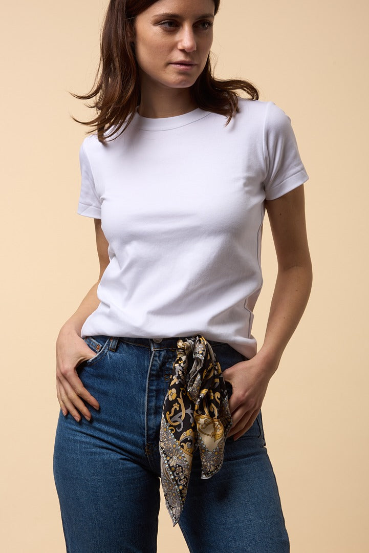brunette woman with jeans, white shirt, and black-gold silk scarf attached to her belt