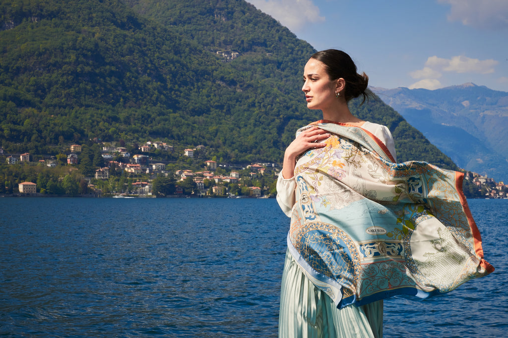 woman dressed with a blue silk scarf, looking over lake Como. On the background lake water, mountains and a lake town