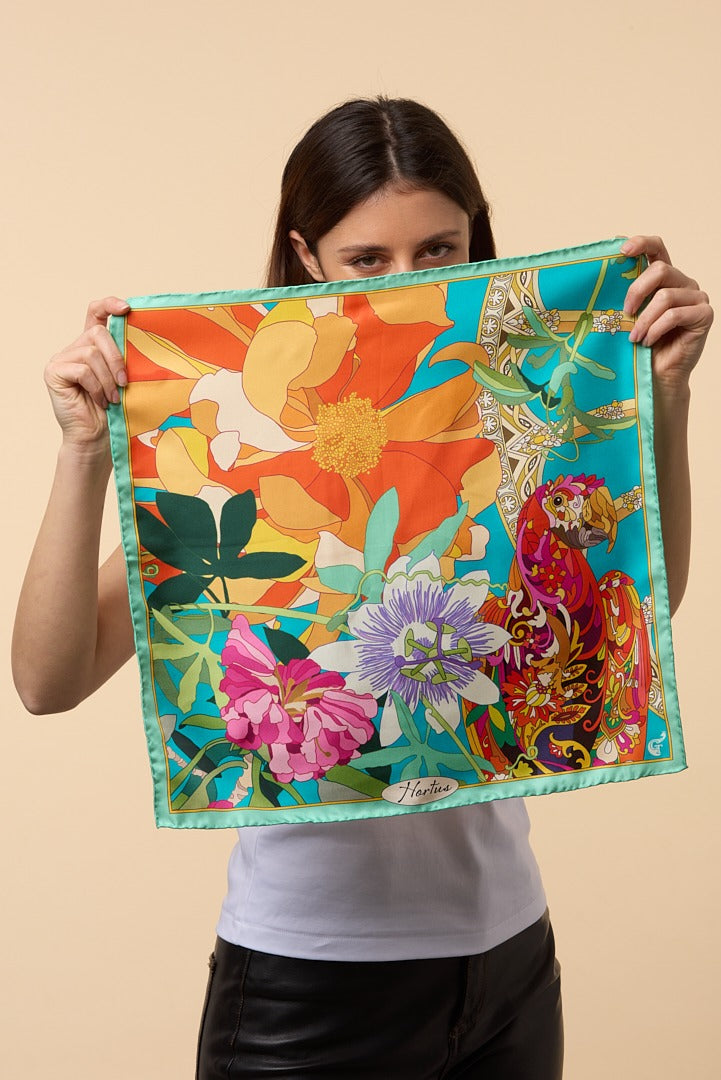 brunette woman holding a colourful silk scarf depicting flowers and a parrot in front of her