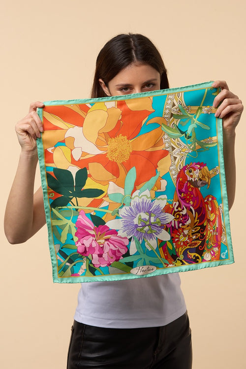 brunette woman holding a colourful silk scarf depicting flowers and a parrot in front of her