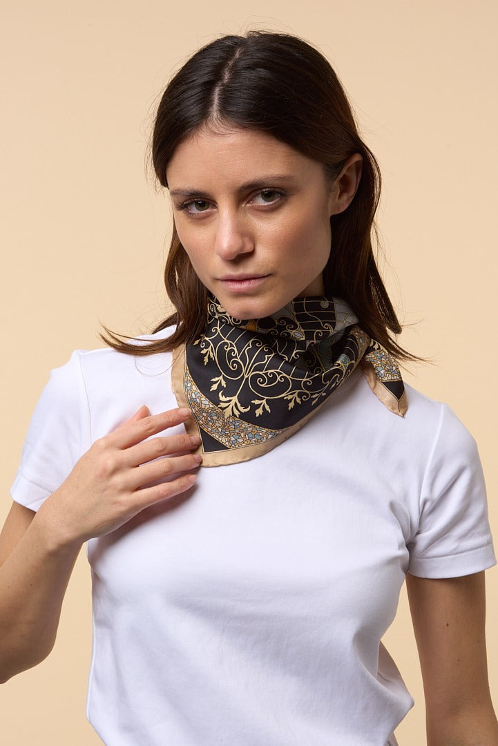brunette woman with white shirt, and black and gold silk scarf on her neck
