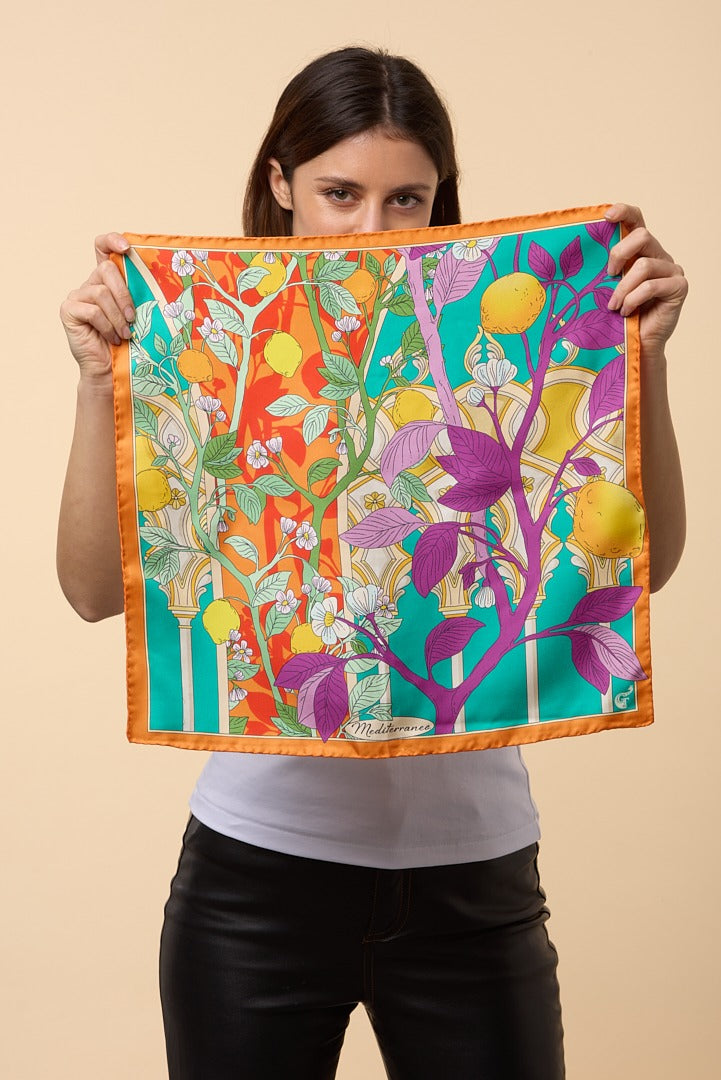 brunette woman holding a colourful silk scarf depicting lemons in front of her 
