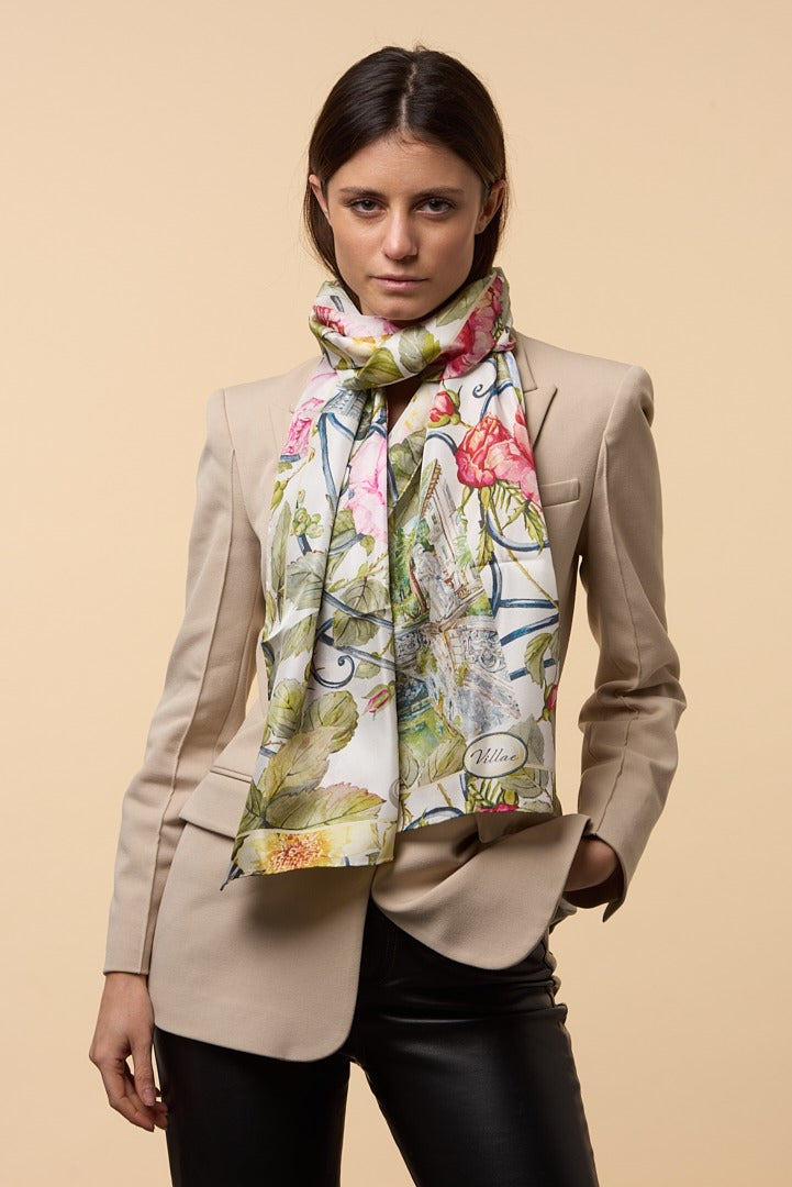 brunette woman with cream jacket, black trousers, and colourful silk scarf depicting flowersand wrought iron gates