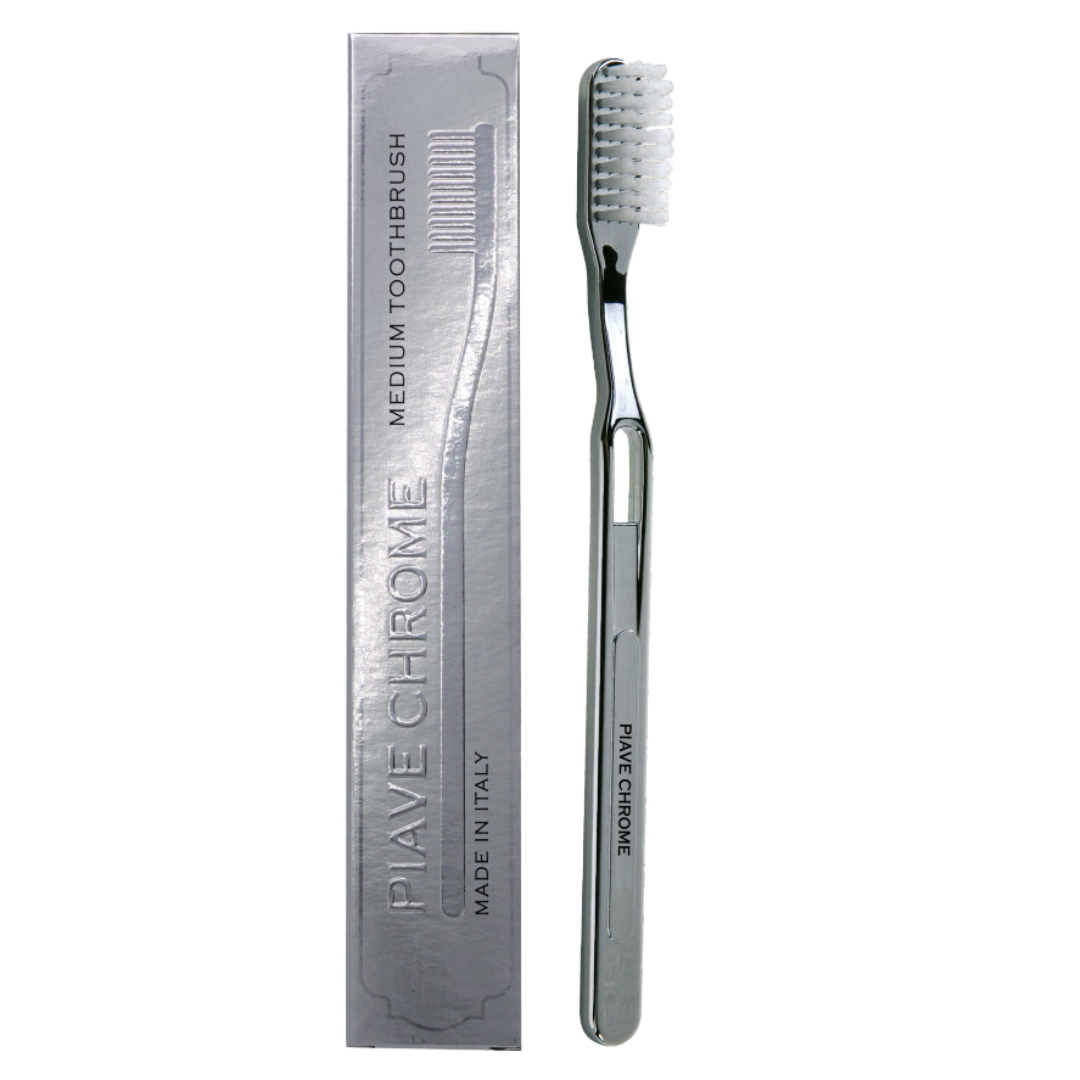 A silver chrome toothbrush with white bristles stands next to its matching metallic gray packaging box on a plain white background. The box is embossed with the brand name 'PIAVE CHROME'.