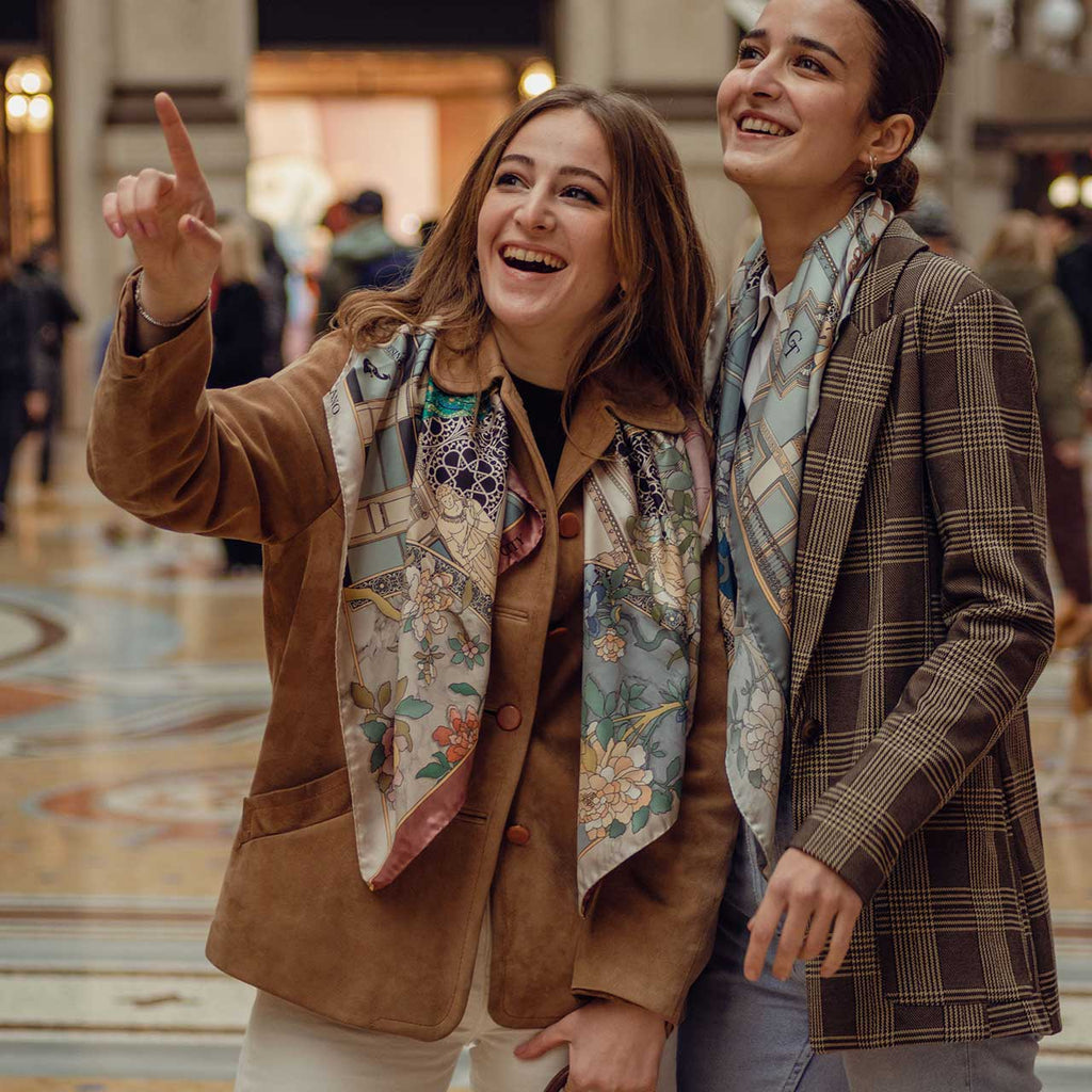 two women laughing inside galleria Vittorio Emanuele in Milan, wearing silk scarves around their neck