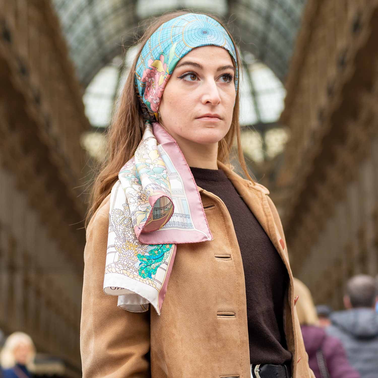 woman standing at the entrance of galleria Vittorio Emanuele in Milan, wearing a brown coat and a silk scarf on her head