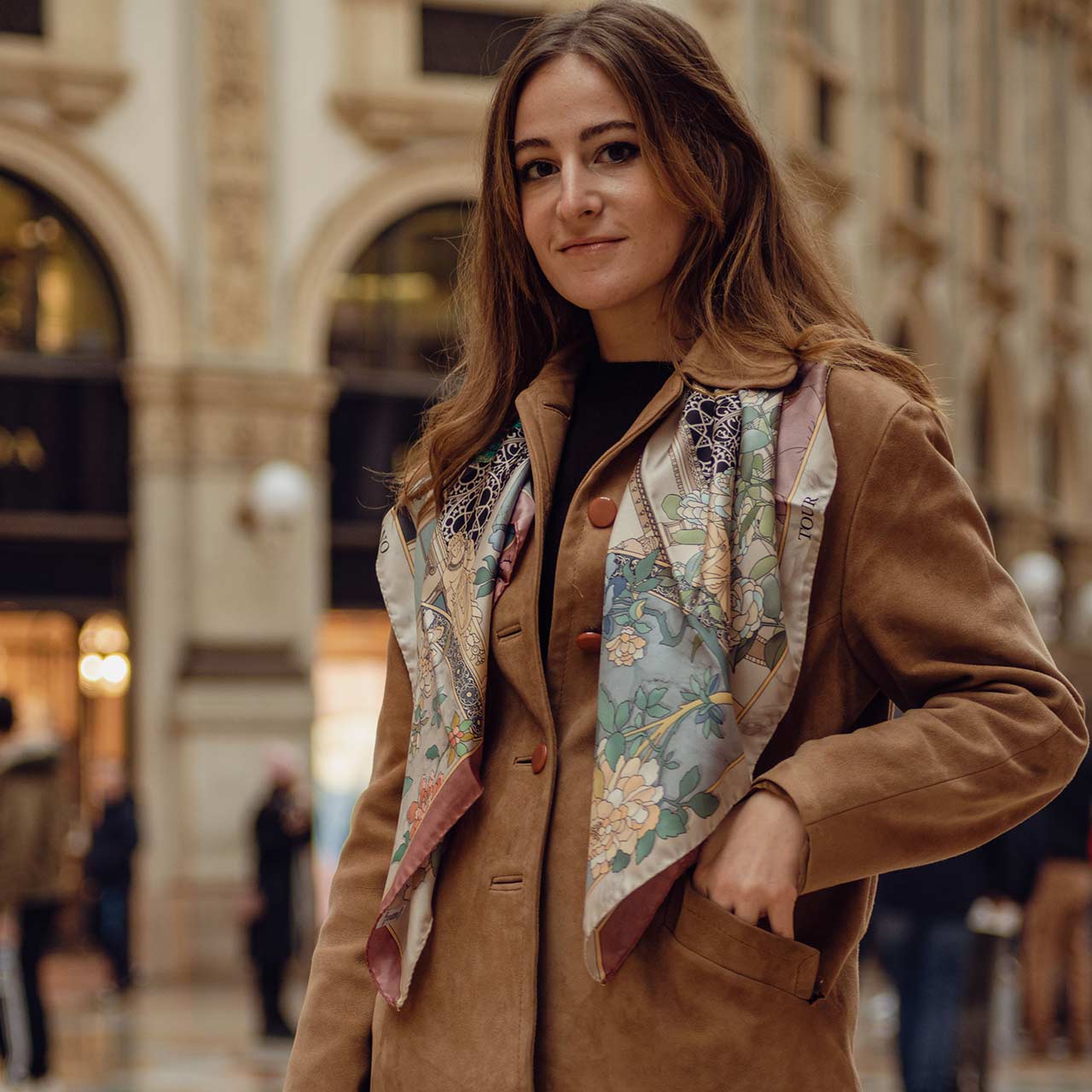 woman standing inside galleria Vittorio Emanuele in Milan, wearing a brown coat and a silk scarf