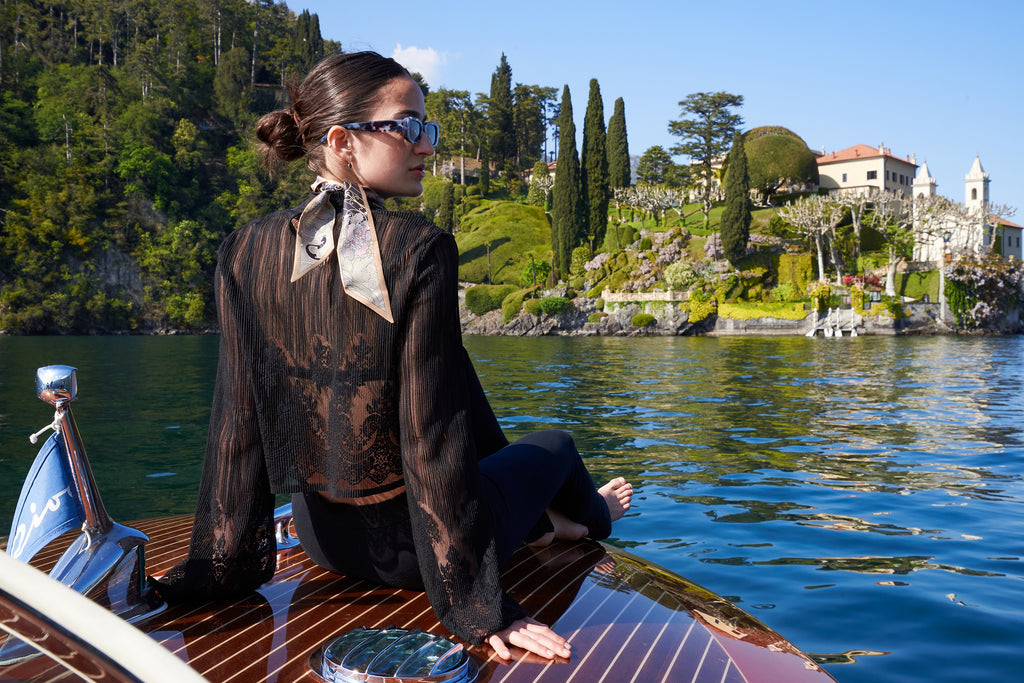 girl with black dress and silk twilly on a motorboat in front of villa Balbianello on lake Como