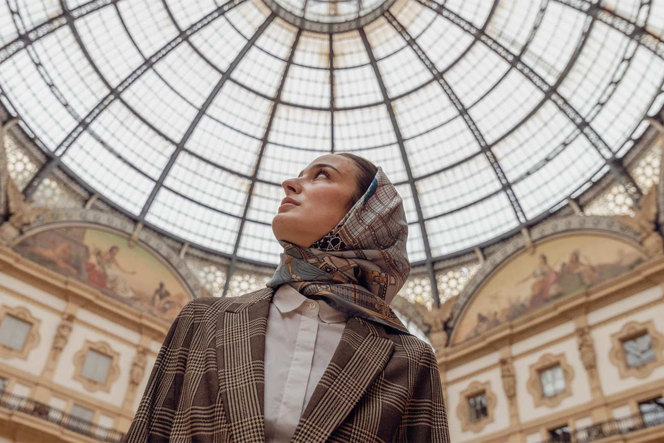 woman wearing a silk scarf on her head, looking up at the glass roof of the galleria Vittorio Emanuele in Milan