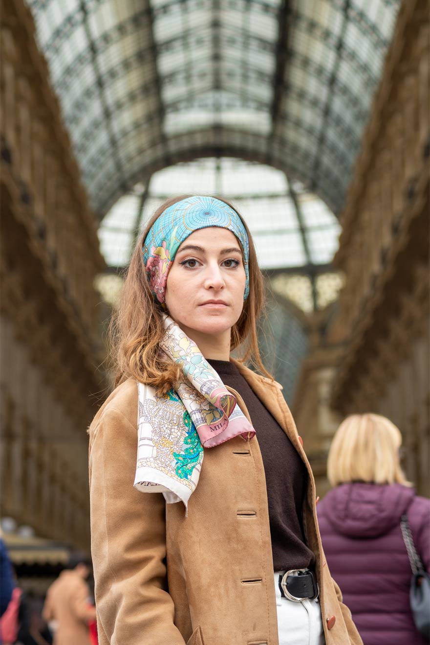 woman standing in front of galleria Vittorio Emanuele in Milan, wearing a brown coat and a silk scarf on her head